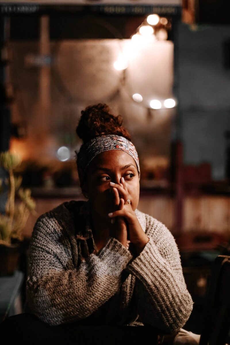 Woman sitting outside with hands on her face, looking thoughtful and reflective during detox and recovery