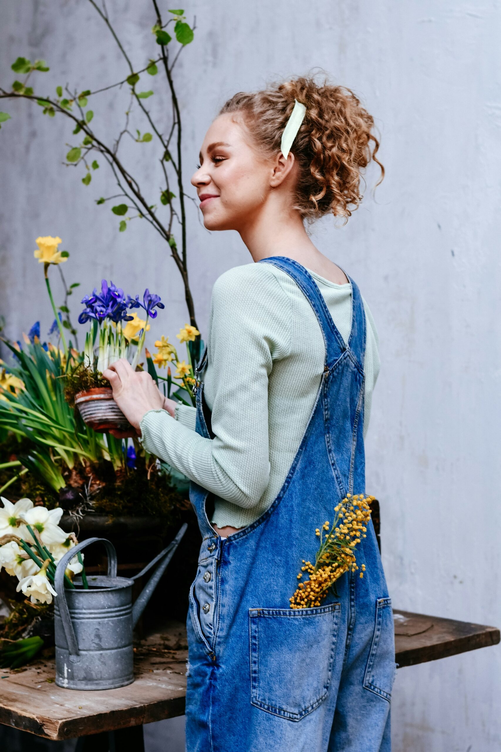 Woman in denim overalls holding a flower pot with flowers in her back pocket, representing holistic healing and natural therapy.